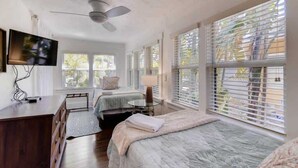 A bedroom with two beds, a ceiling fan, a TV, and large windows with blinds. - The Periwinkle House – Bask Poolside at this Sunlit West Palm Retreat (West Palm Beach)