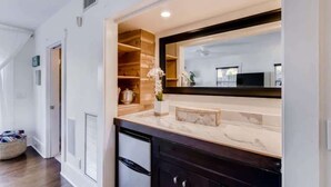 A modern kitchen with a marble countertop, a built-in oven, and a large mirror above the sink. - The Periwinkle House – Bask Poolside at this Sunlit West Palm Retreat (West Palm Beach)
