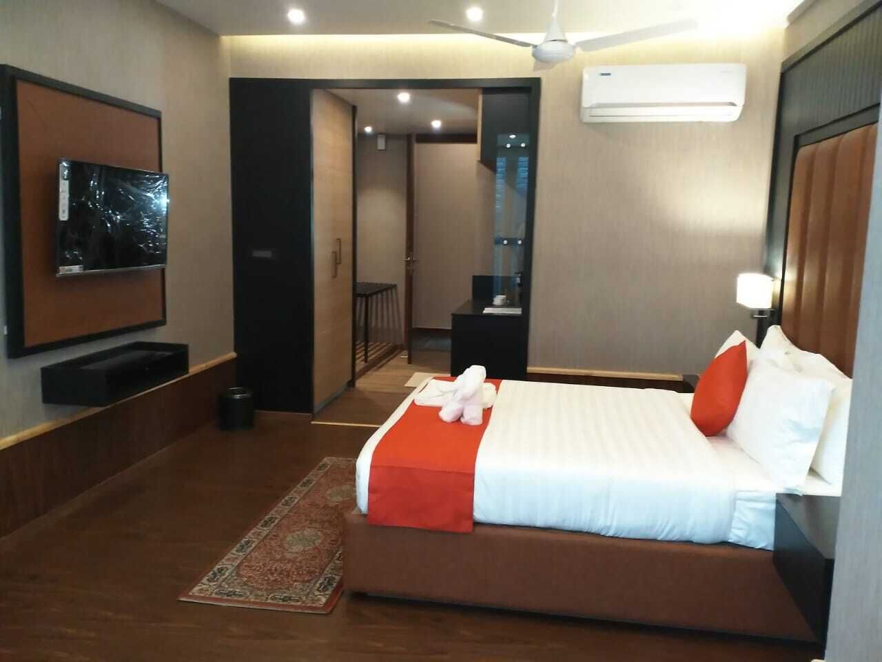Habitación de hotel con una cama grande, un televisor de pantalla plana montado en la pared, un aire acondicionado y un ventilador de techo.