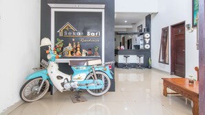 A reception area with a sign for 'Sekar Sari Residence', a blue scooter, a wooden bench, and a modern interior with a staircase.