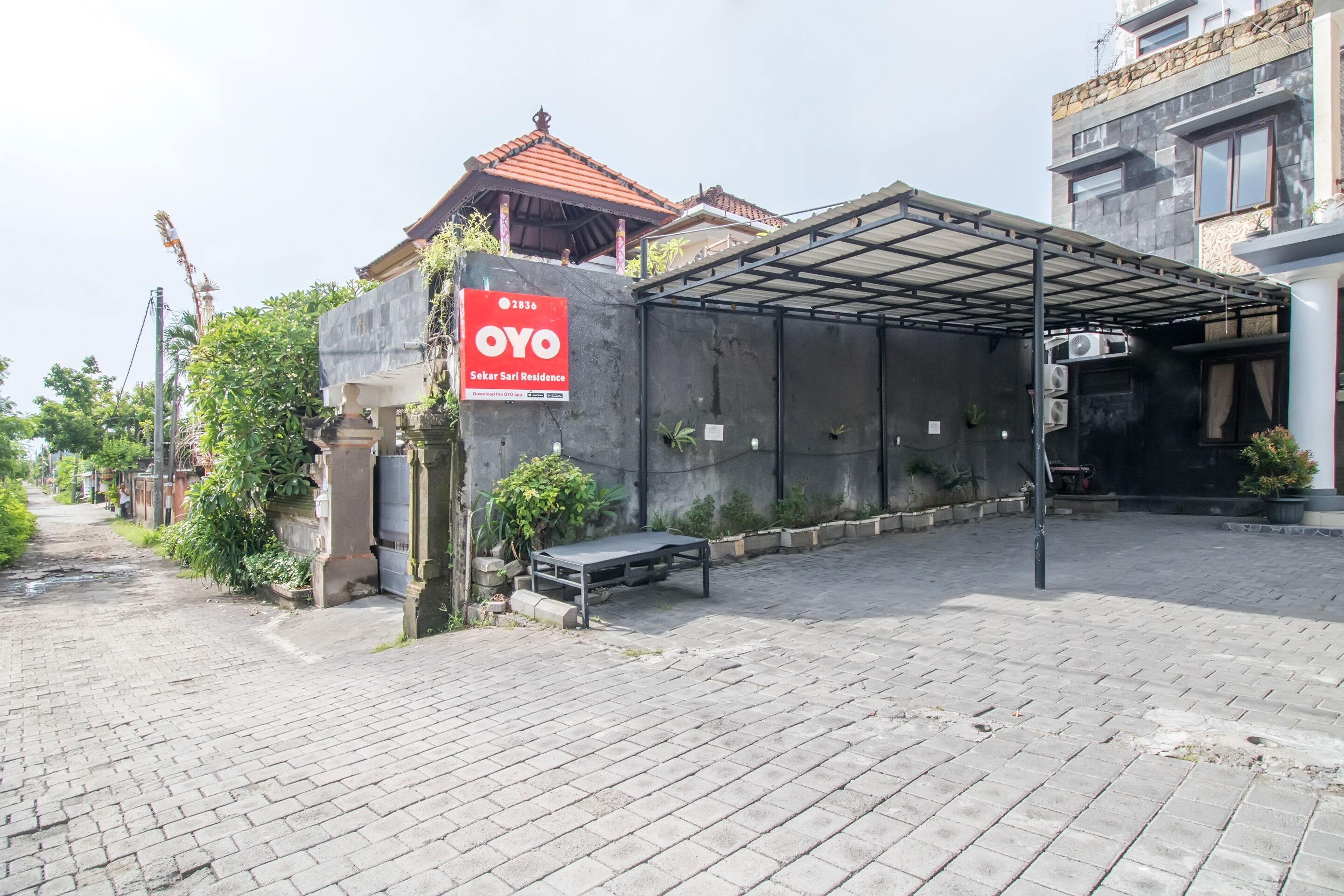 A residential area with a sign for OYO Sekar Sari Residence, a covered outdoor area, and a paved walkway.
