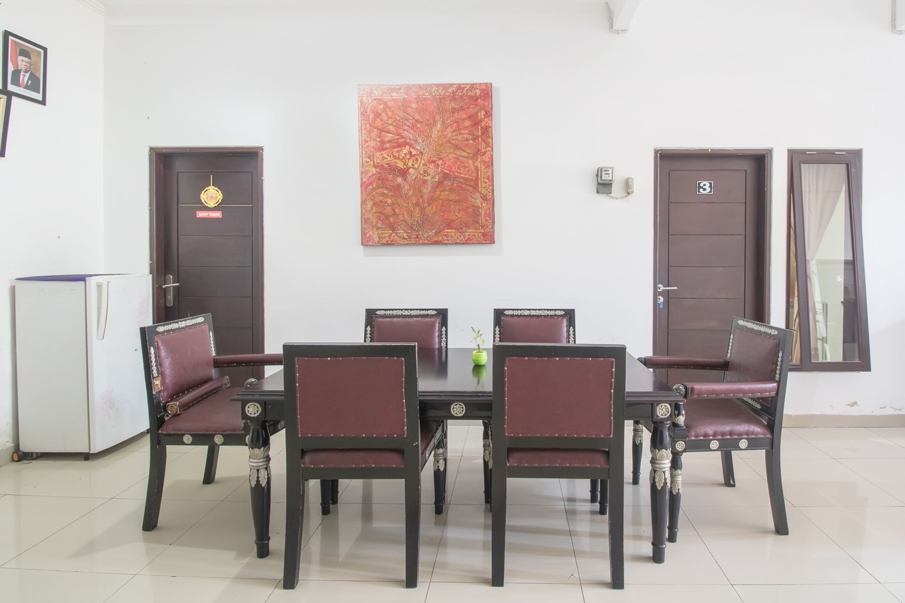 Un comedor con una mesa y sillas a juego de madera oscura, un cuadro decorativo grande en la pared y dos puertas con números.