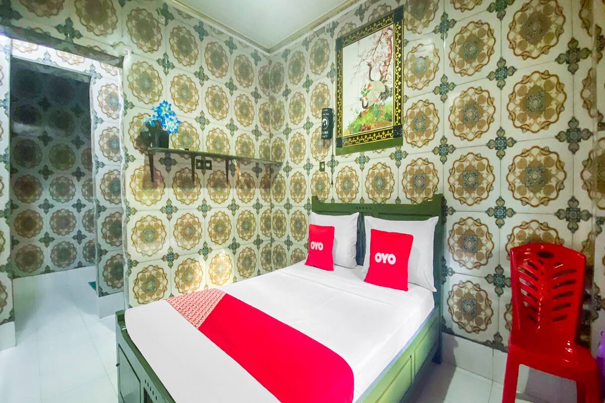 Quarto com cama, uma cadeira vermelha e papel de parede estampado.