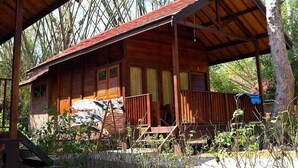 A wooden cabin with a porch, a covered area, and a vehicle parked outside.