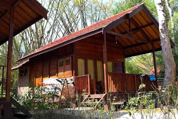 A wooden cabin with a porch, a covered area, and a vehicle parked outside.