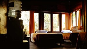 A room with two beds, a large water dispenser, and large windows with curtains.