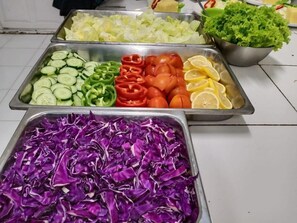 A buffet with various vegetables including cucumbers, bell peppers, tomatoes, and cabbage.