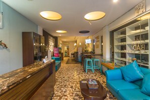 Un vestíbulo de hotel con un mostrador de recepción, un sofá azul, una mesa de centro y una vitrina de vidrio con vajilla.
