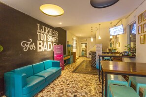 A hotel lobby with a blue sofa, a tiled floor, a television, and a wall with motivational text. - OYO 2544 Just-in Hotel (Mataram)