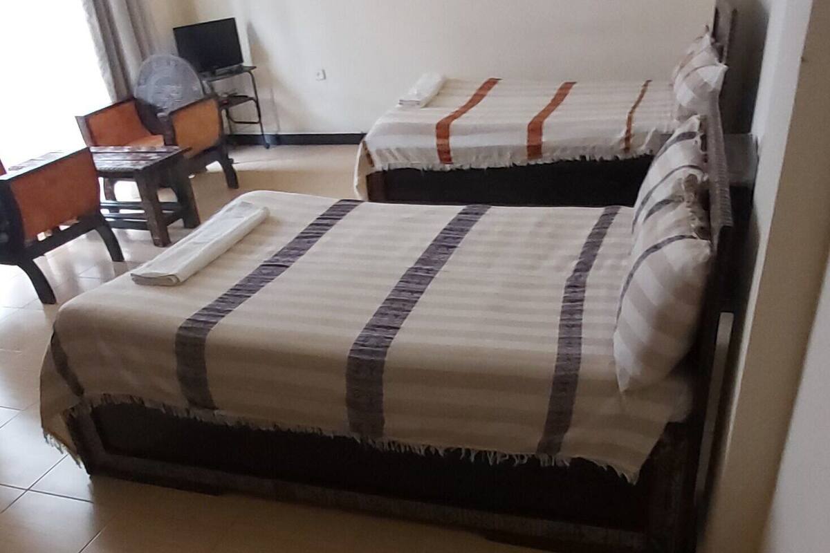 A hotel room with two beds, a desk, a chair, a TV, and a window with curtains.
