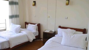 A hotel room with two single beds, a small bedside table, and a nightstand.