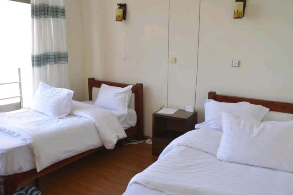 A hotel room with two single beds, a small bedside table, and a nightstand.