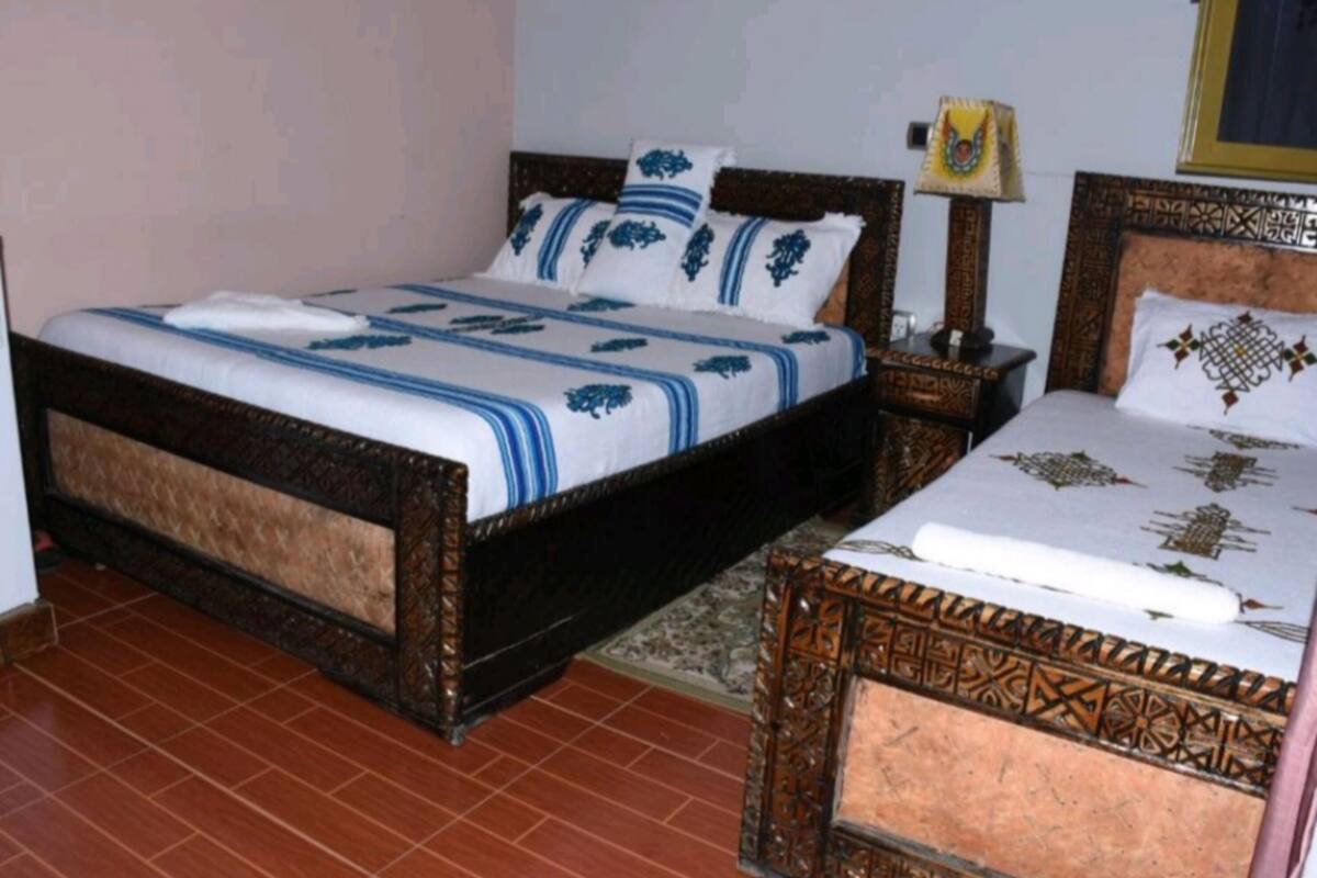 A bedroom with a large bed, a smaller bed, a nightstand, and a lamp.