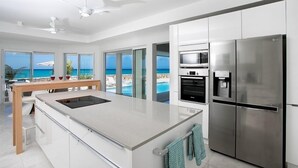 A modern kitchen with a large island, stainless steel appliances, and a view of the ocean. - Villa Ecume Des Jours (Les Terres Basses)
