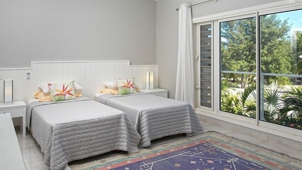 A bedroom with two beds, a large window with a view of greenery, and a patterned rug. - Villa Ecume Des Jours (Les Terres Basses)