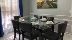 A dining area with a glass table, black chairs, and a painting of a sunset beach scene. - 6183 Sandcrest · Walk TO Universal! Near Disney, Convention (Orlando)