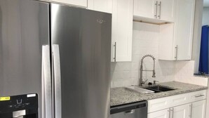 A kitchen with stainless steel appliances, a water dispenser, a granite countertop, and white cabinetry. - 6183 Sandcrest · Walk TO Universal! Near Disney, Convention (Orlando)