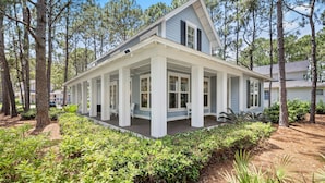 A two-story house with a covered porch, surrounded by trees and greenery.
