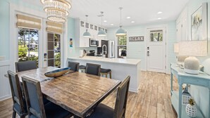 A modern kitchen with a wooden dining table, pendant lights, and a view of the outdoors.