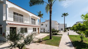 A residential building with a tiled roof, a balcony, and a paved pathway. - Fig Tree Z Holiday Villas DPS04-Two Bed Townhouse (Protaras)