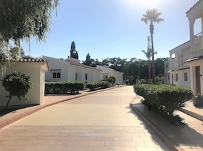 A paved walkway leading to a white building with multiple windows and a tiled roof.