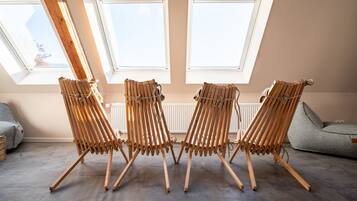 Una habitación con tres sillas de madera alineadas, un sofá gris y una ventana que da al cielo.