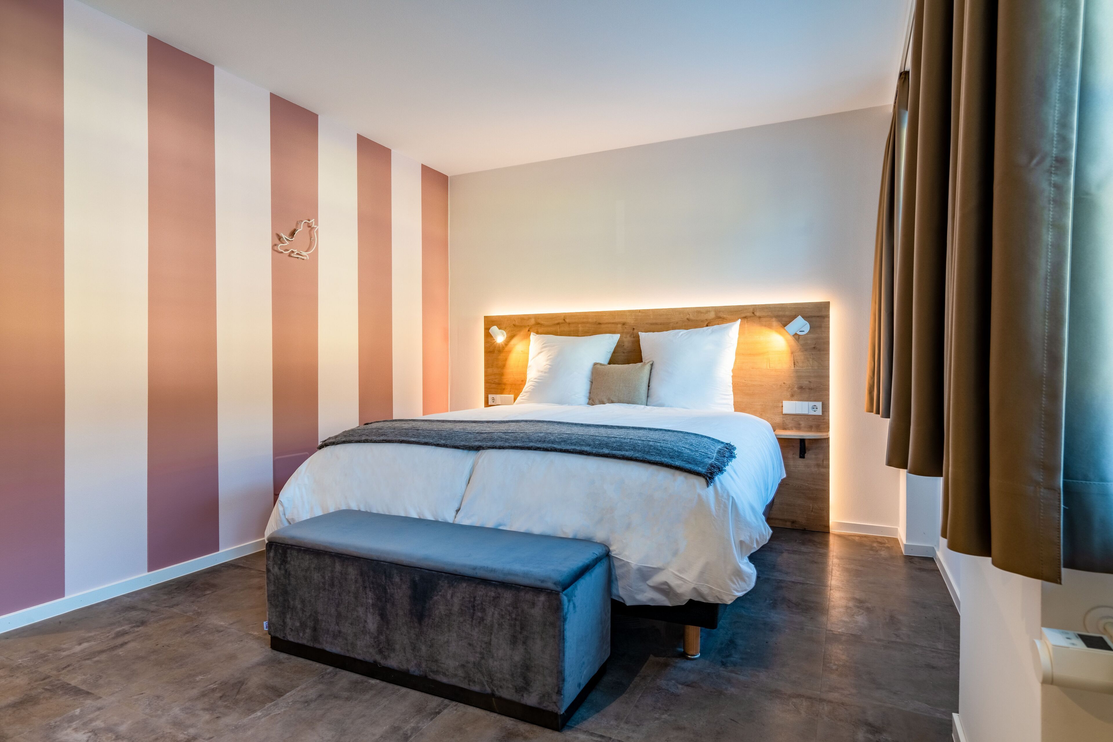 A modern hotel room with a large bed, a bench, and a wooden headboard.