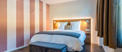A modern hotel room with a large bed, a bench, and a wooden headboard.