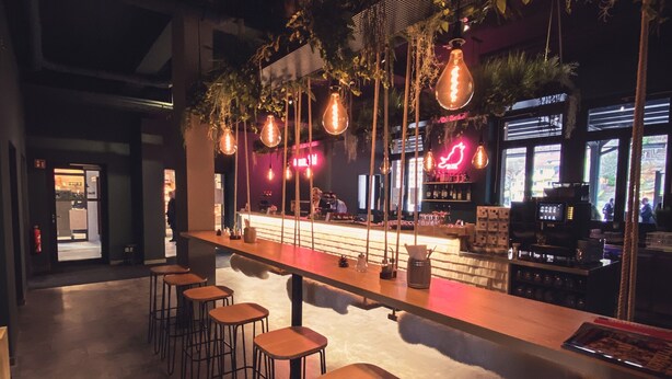 Un espace bar avec des tabourets en bois, des suspensions décoratives et un comptoir équipé du matériel nécessaire.