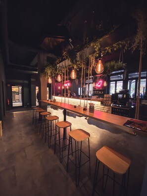Zona de bar con taburetes de madera, luces colgantes y una barra equipada.
