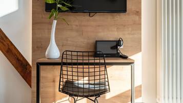 Ein moderner Arbeitsbereich mit einem Holztisch, einem schwarzen Stuhl, einer weißen Vase mit Pflanze, einem Wand-Fernseher und einer Heizung.