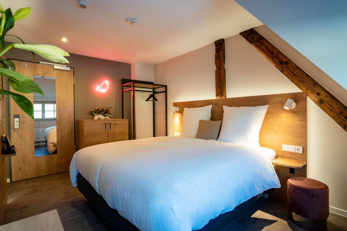 A modern bedroom with a large bed, wooden headboard, bedside tables, and a hanging light fixture.
