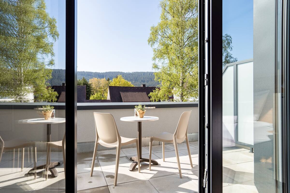 A balcony with two tables and chairs, overlooking a forested area.