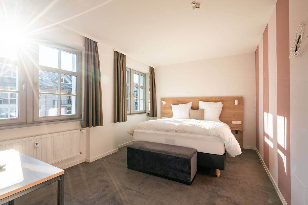 A modern bedroom with a large bed, a small table, and a window with curtains.