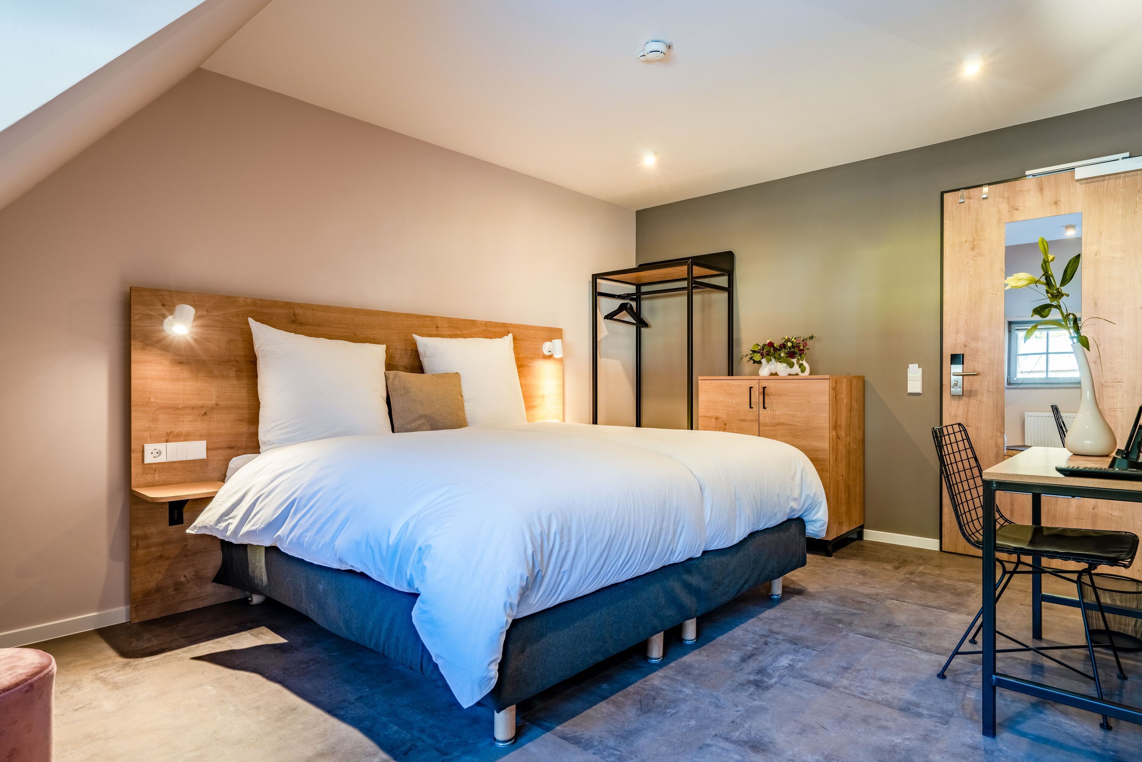 A modern bedroom with a large bed, wooden headboard, bedside tables, a desk with a chair, and a wardrobe.