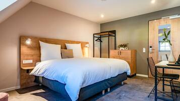 A modern bedroom with a large bed, wooden headboard, bedside tables, a desk with a chair, and a wardrobe.