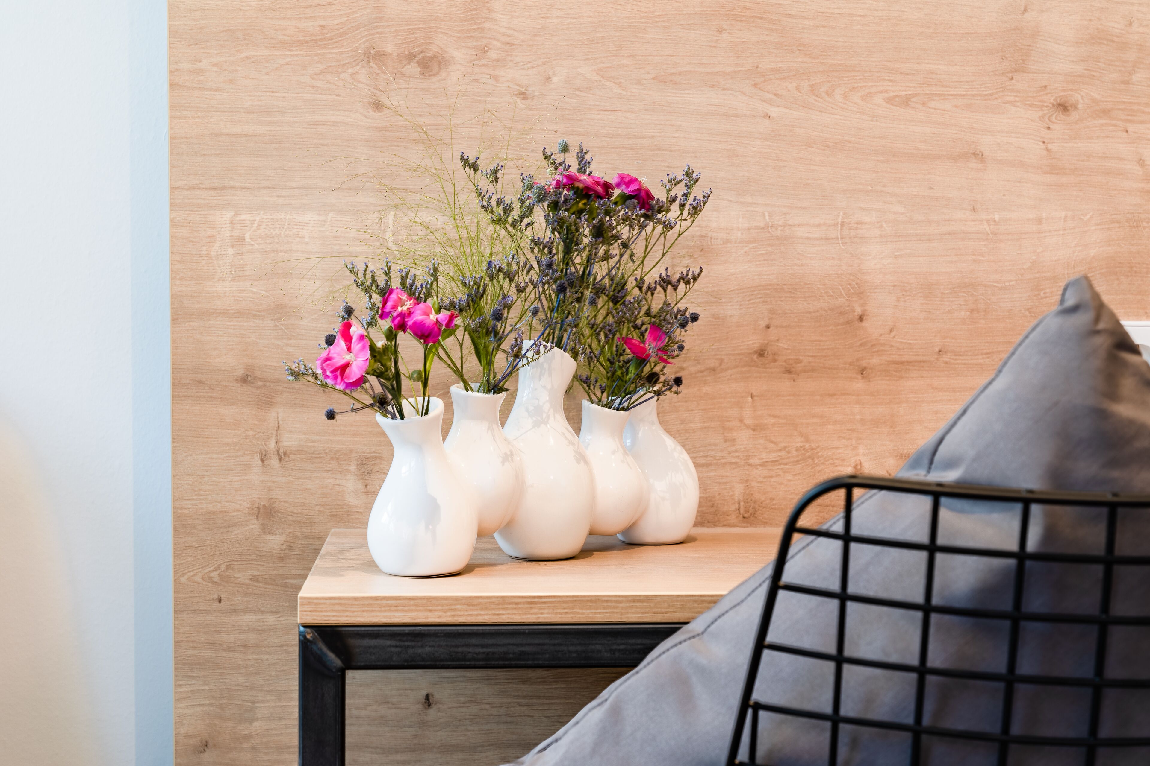 Una mesita de noche de madera con cuatro jarrones blancos que contienen flores rosas y follaje.