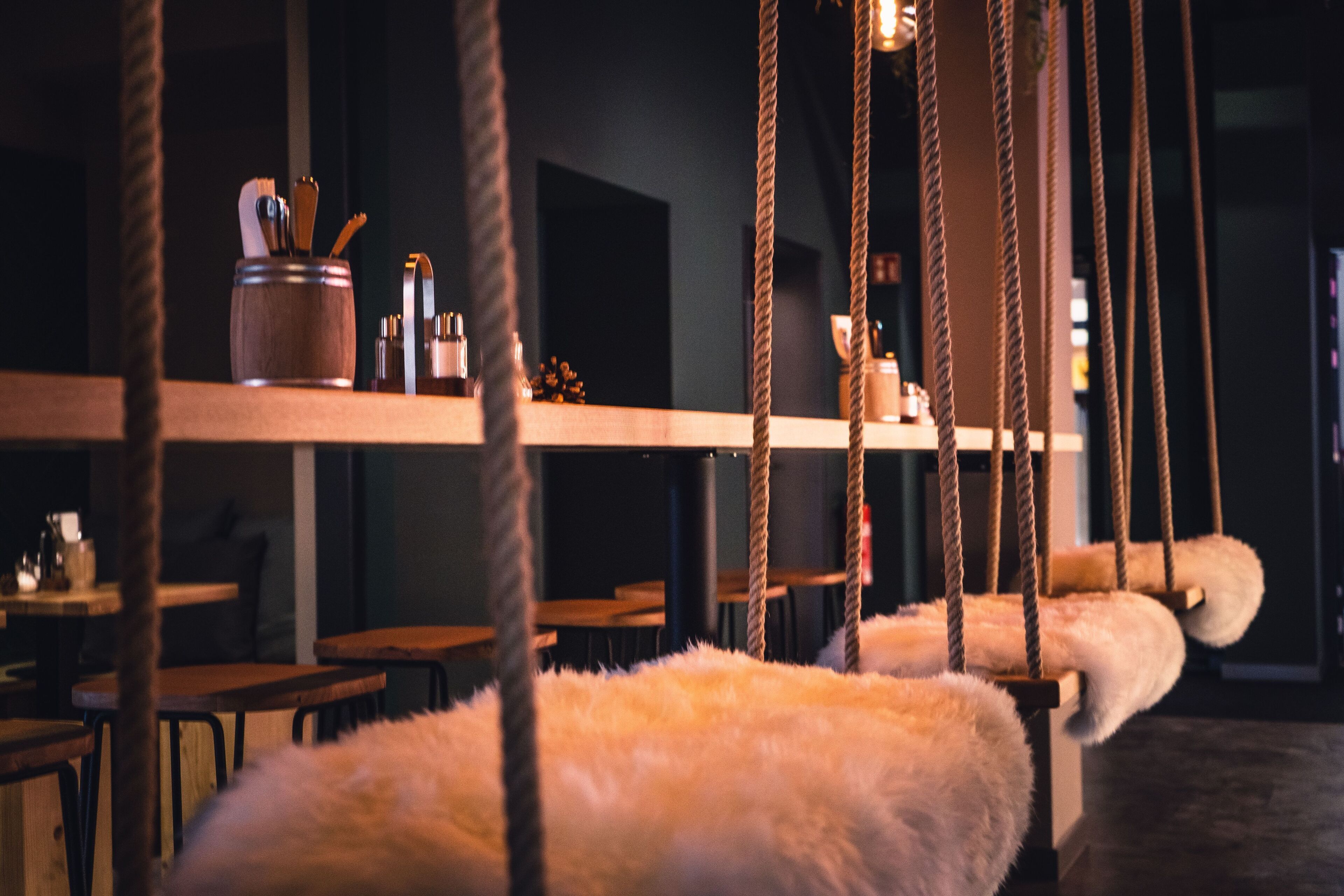 A cozy indoor setting with wooden tables and chairs, a hanging rope swing, and a fluffy white object.