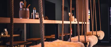 Un ambiente interior acogedor con mesas y sillas de madera, un columpio de cuerda colgante y un objeto blanco mullido.
