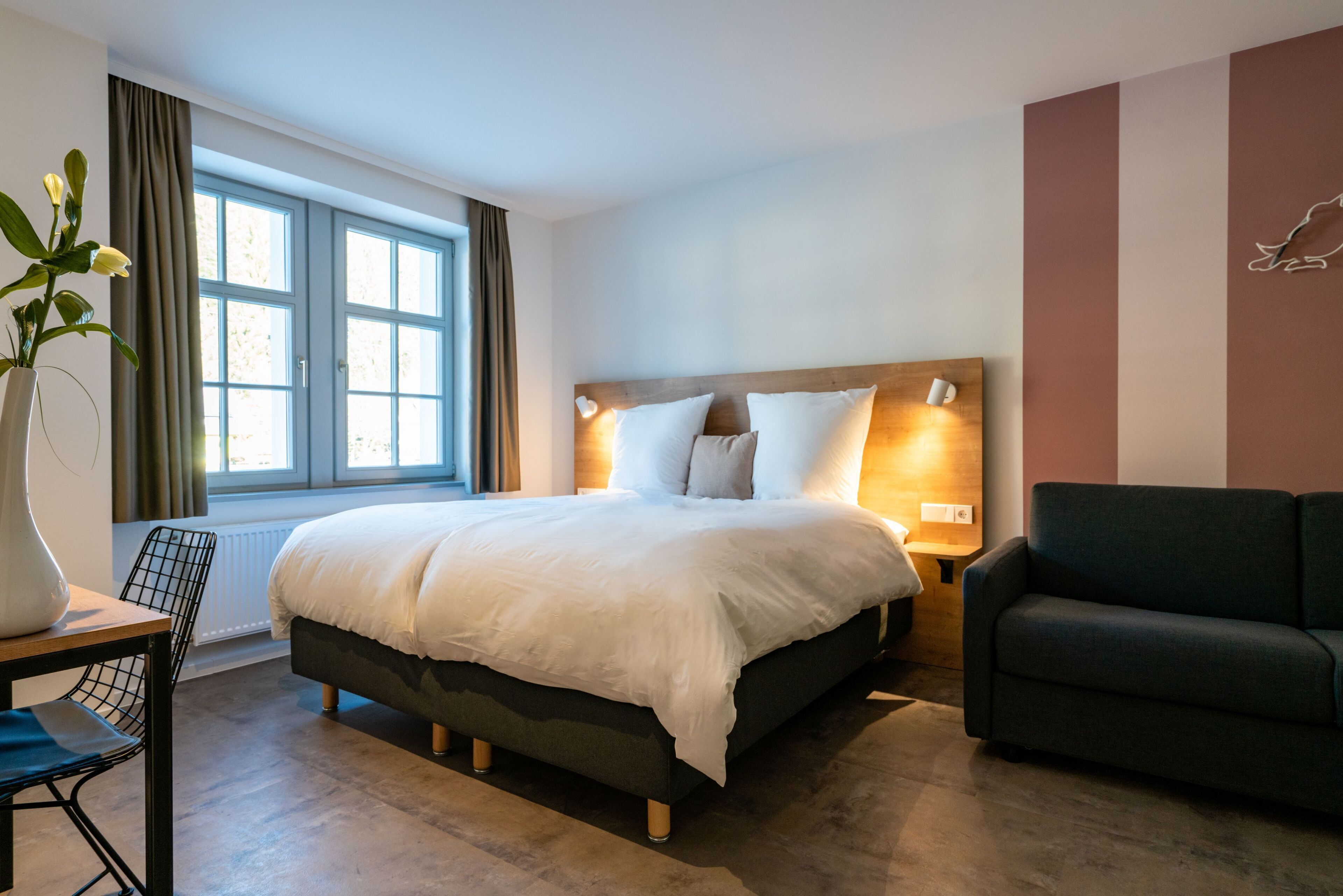 Een moderne hotelkamer met een groot bed, nachtkastje, stoel en een sofa.