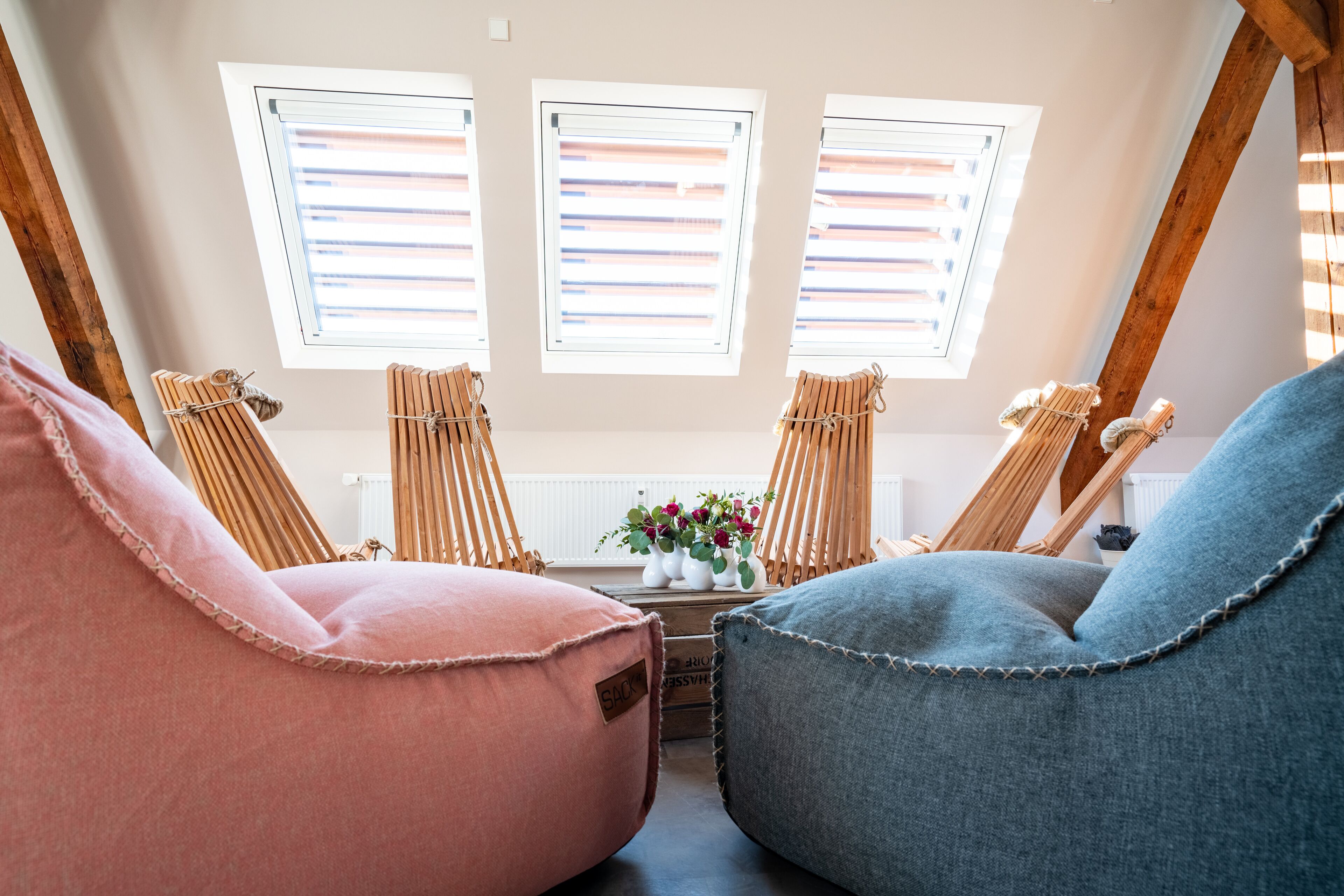 A cozy loft bedroom with a sloped ceiling, three windows with blinds, and two bean bag chairs.