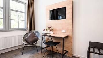 A modern room with a wooden desk, two chairs, a TV mounted on the wall, and a window with curtains.