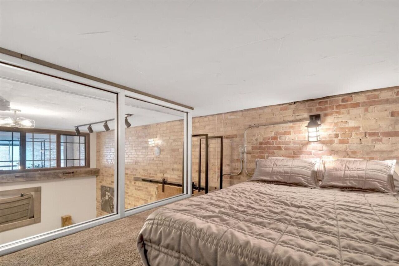 Une chambre avec un grand lit, un mur en briques et une porte vitrée donnant sur un balcon.