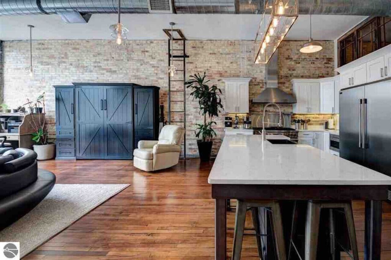 A modern kitchen with a large island, white cabinets, and a brick wall.