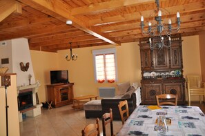 Un salon chaleureux avec une cheminée, un téléviseur, une table à manger avec des chaises et un plafond en bois.