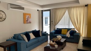 A modern living room with two blue sofas, a coffee table, and a large window with curtains.