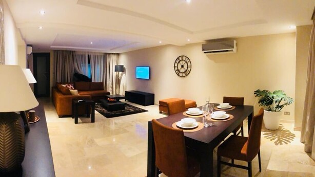 A modern living room with a dining area, a flat-screen TV mounted on the wall, and a large potted plant.