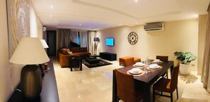 Una sala de estar moderna con comedor, un televisor de pantalla plana en la pared y una planta grande en maceta.