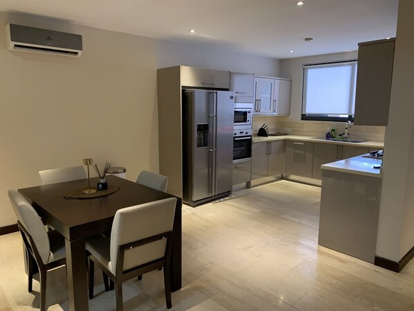 Una cocina moderna con zona de comedor, que cuenta con electrodomésticos de acero inoxidable, horno empotrado y una ventana sobre el fregadero.