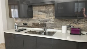 A modern kitchen with dark cabinets, a stainless steel sink, a stone backsplash, and a purple toaster.